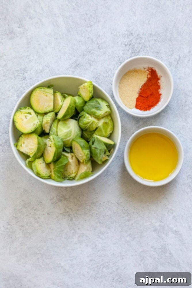 Crispy Garlic Roasted Brussels 5 An overhead shot showcasing fresh Brussels sprouts, a bottle of olive oil, and small bowls of garlic powder, garlic salt, and paprika on a wooden surface, ready for preparation.