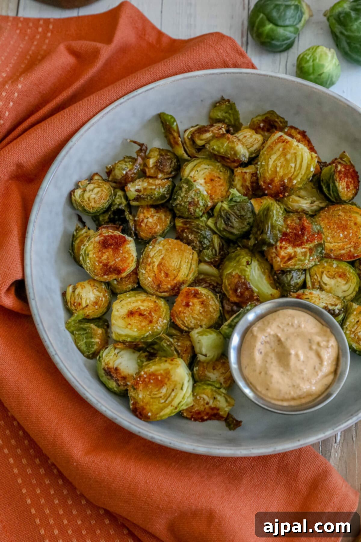 Crispy Garlic Roasted Brussels 9 A serving of roasted Brussels sprouts with garlic and a side of dipping sauce in a clean white bowl, ready to be enjoyed.