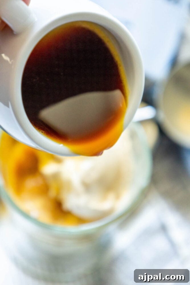 A hand carefully pouring a shot of hot espresso over two scoops of Earl Grey ice cream in a glass.