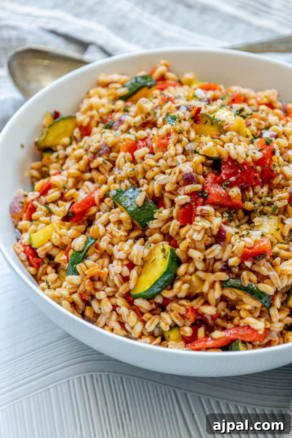 Vibrant Farro Salad with Zucchini and Bell Pepper 2 Delicious farro salad featuring zucchini, red onion, roasted red pepper, and fresh herbs, served in an elegant white bowl on a rustic wooden table.
