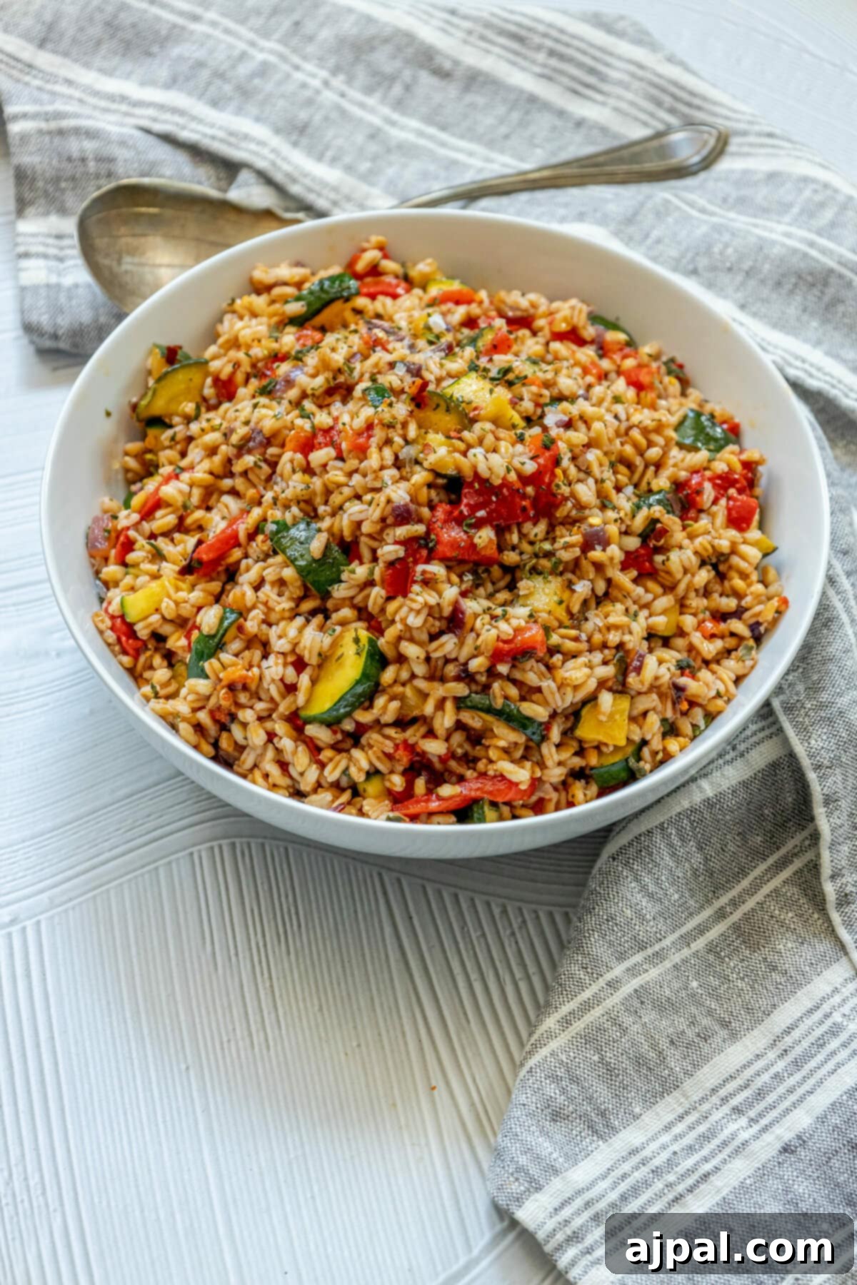 Vibrant Farro Salad with Zucchini and Bell Pepper 4 Vegan Red Pepper Zucchini Farro Salad served in a white bowl with a spoon, highlighting its vibrant ingredients.