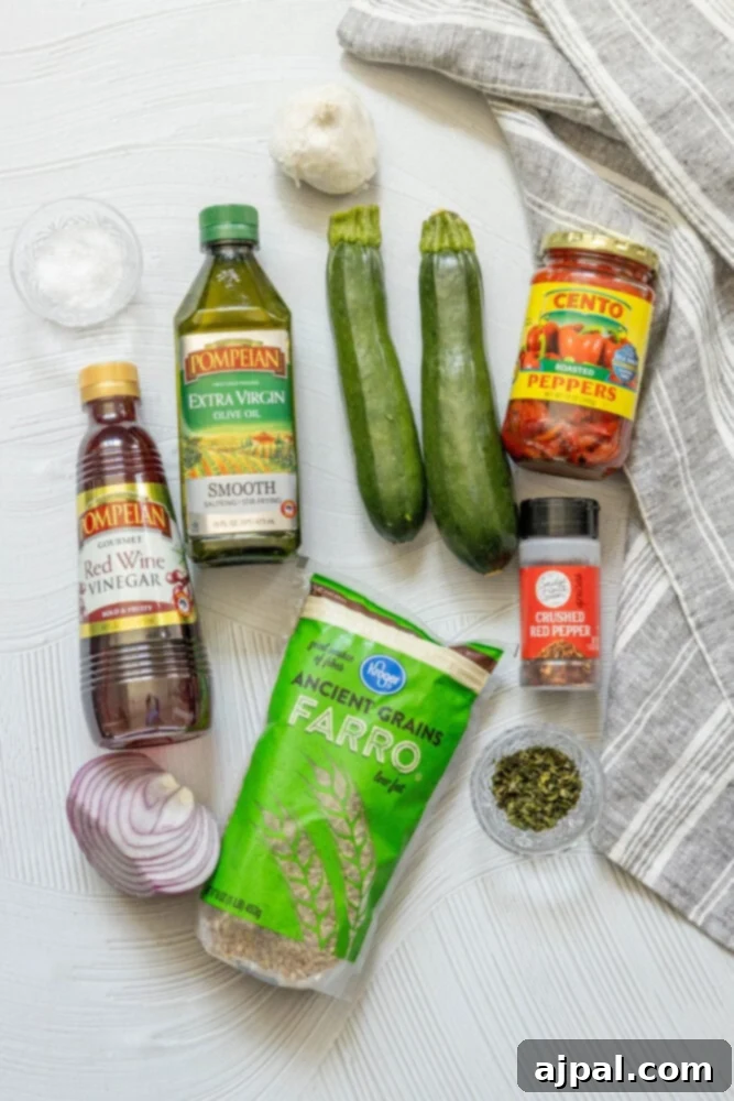 Vibrant Farro Salad with Zucchini and Bell Pepper 5 Ingredients for a Red Pepper Zucchini Farro Salad laid out on a table, including fresh zucchini, tomatoes, and onions.