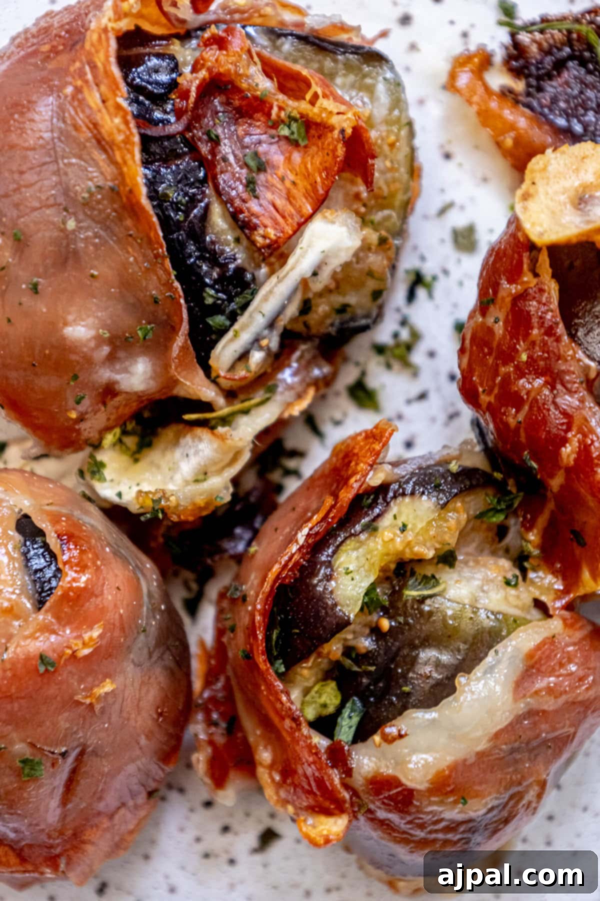 Gourmet Fig, Prosciutto, and Brie Bites 2 Fig stuffed with brie and wrapped in prosciutto on a plate with fresh chives