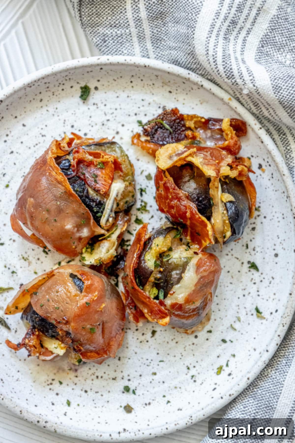 Gourmet Fig, Prosciutto, and Brie Bites 3 Baked figs stuffed with brie and prosciutto on a white plate with fresh chives