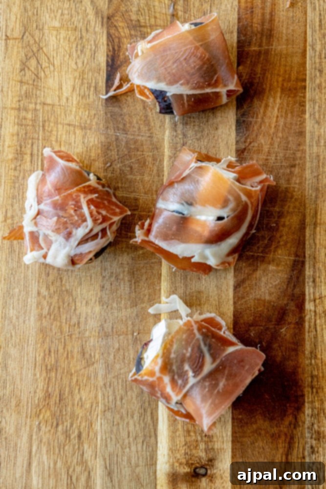 Gourmet Fig, Prosciutto, and Brie Bites 7 Picture of several stuffed figs with brie, wrapped in raw prosciutto, arranged on a baking sheet