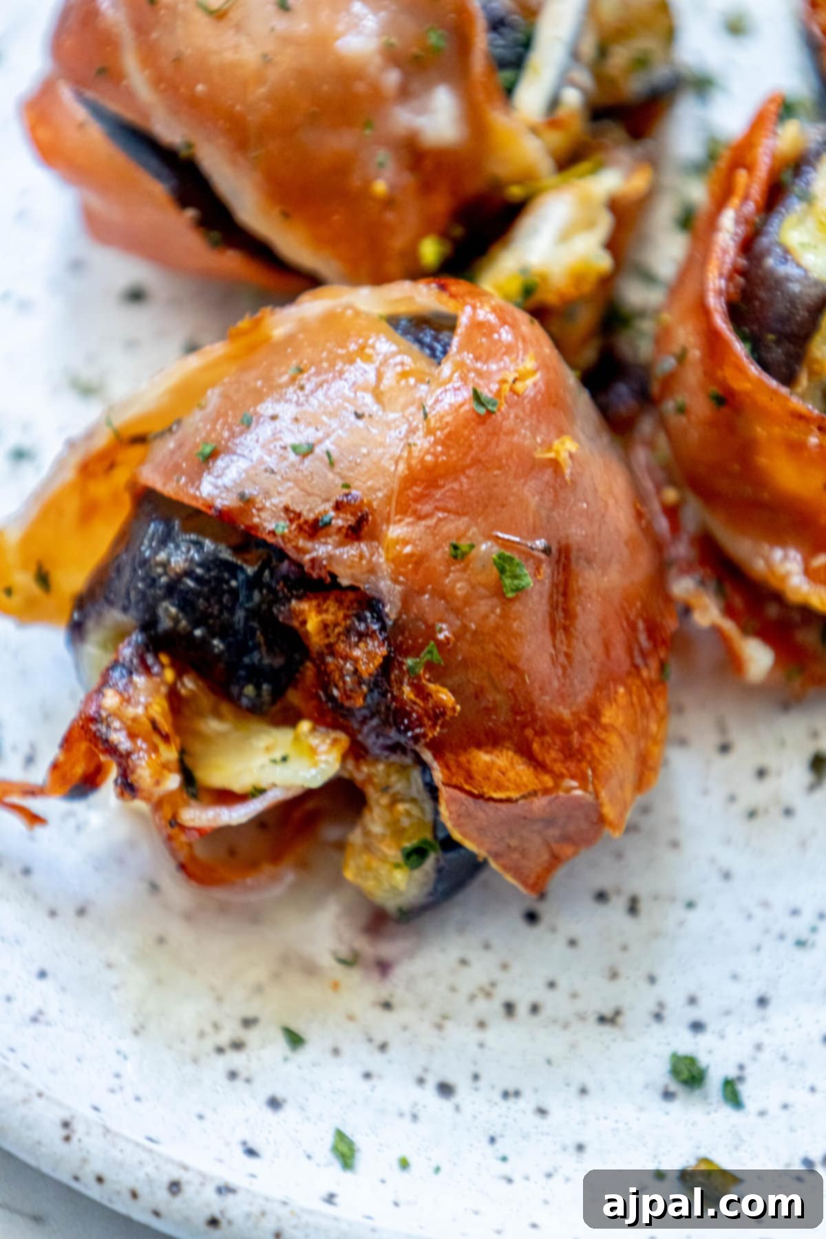 Gourmet Fig, Prosciutto, and Brie Bites 10 Brie-stuffed prosciutto figs beautifully arranged on a plate with fresh herbs