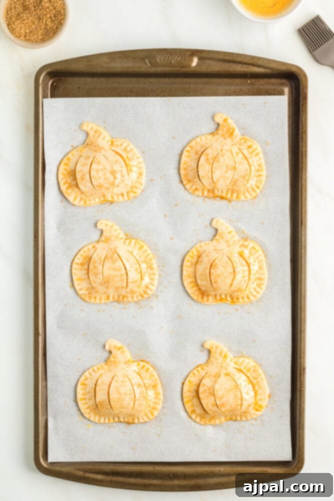 Autumn Pumpkin Pockets 11 An unbaked pumpkin-shaped hand pie, with crimped edges and decorative slits, resting on parchment paper on a baking sheet.