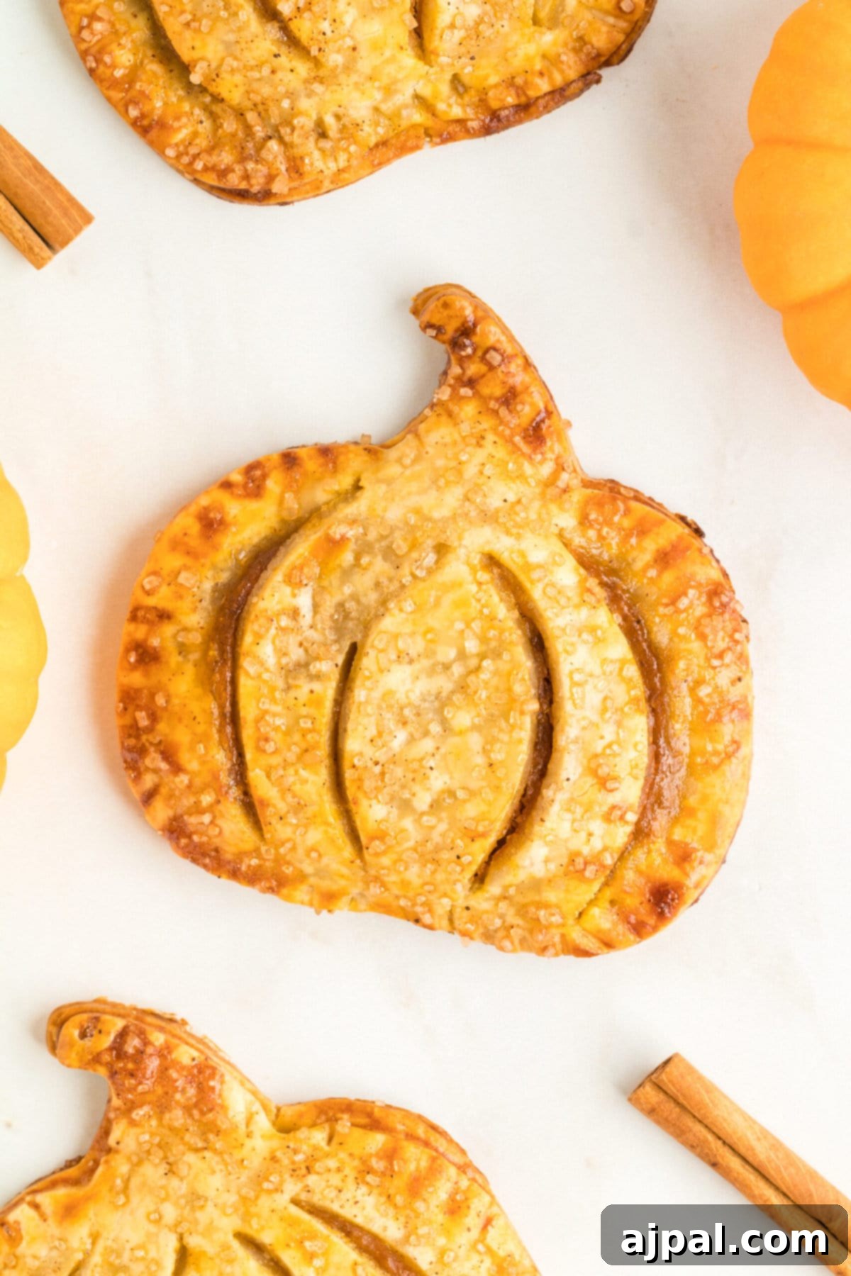 Autumn Pumpkin Pockets 12 Several golden pumpkin-shaped hand pies arranged on a wooden table, adorned with cinnamon sticks and small decorative pumpkins.