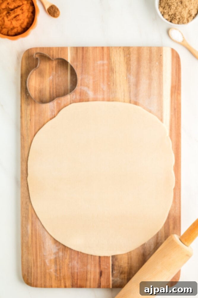 Autumn Pumpkin Pockets 6 A rolling pin and a pumpkin-shaped cookie cutter on a sheet of pie dough, ready for cutting.