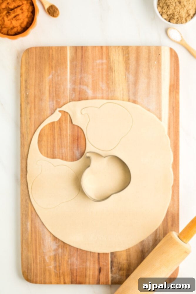 Autumn Pumpkin Pockets 7 A pumpkin-shaped cookie cutter pressing down on pie dough, beginning to form a hand pie shape.