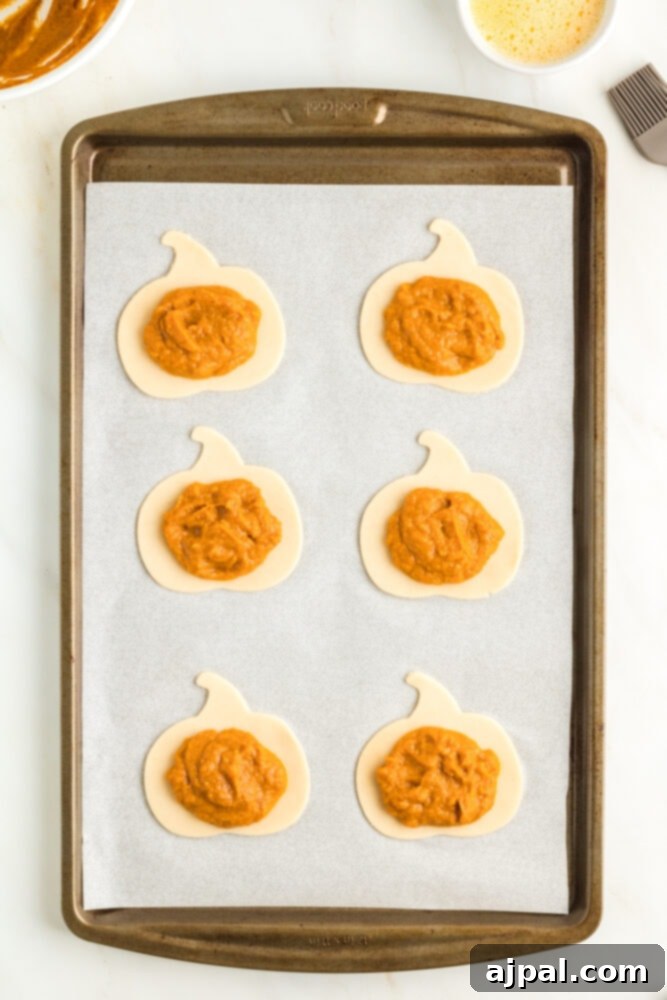 Autumn Pumpkin Pockets 9 A spoon carefully placing spiced pumpkin pie filling onto a pumpkin-shaped piece of pie dough.