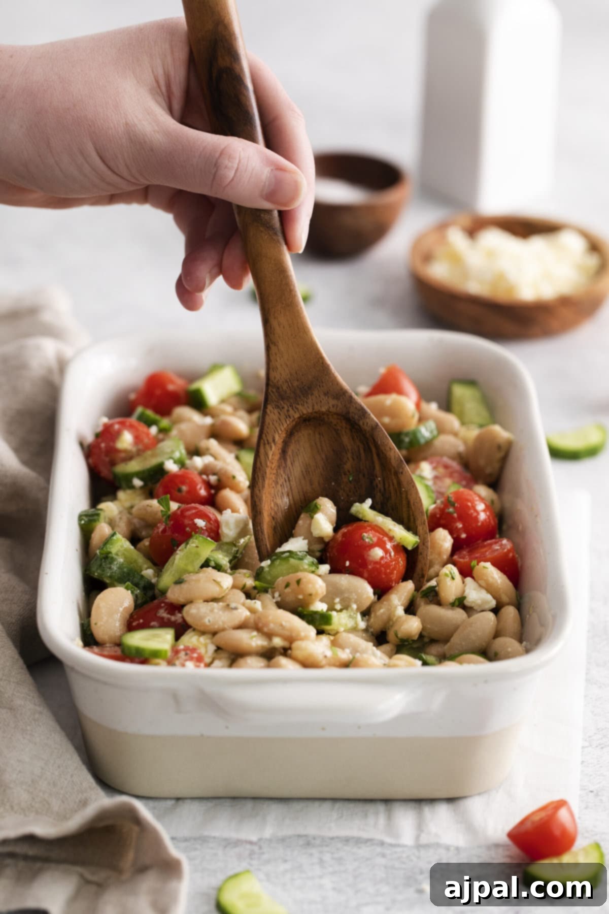 A beautifully presented Mediterranean white bean salad in a white bowl, garnished with fresh cucumber slices, juicy cherry tomatoes, and crumbled feta cheese, ready to be enjoyed.