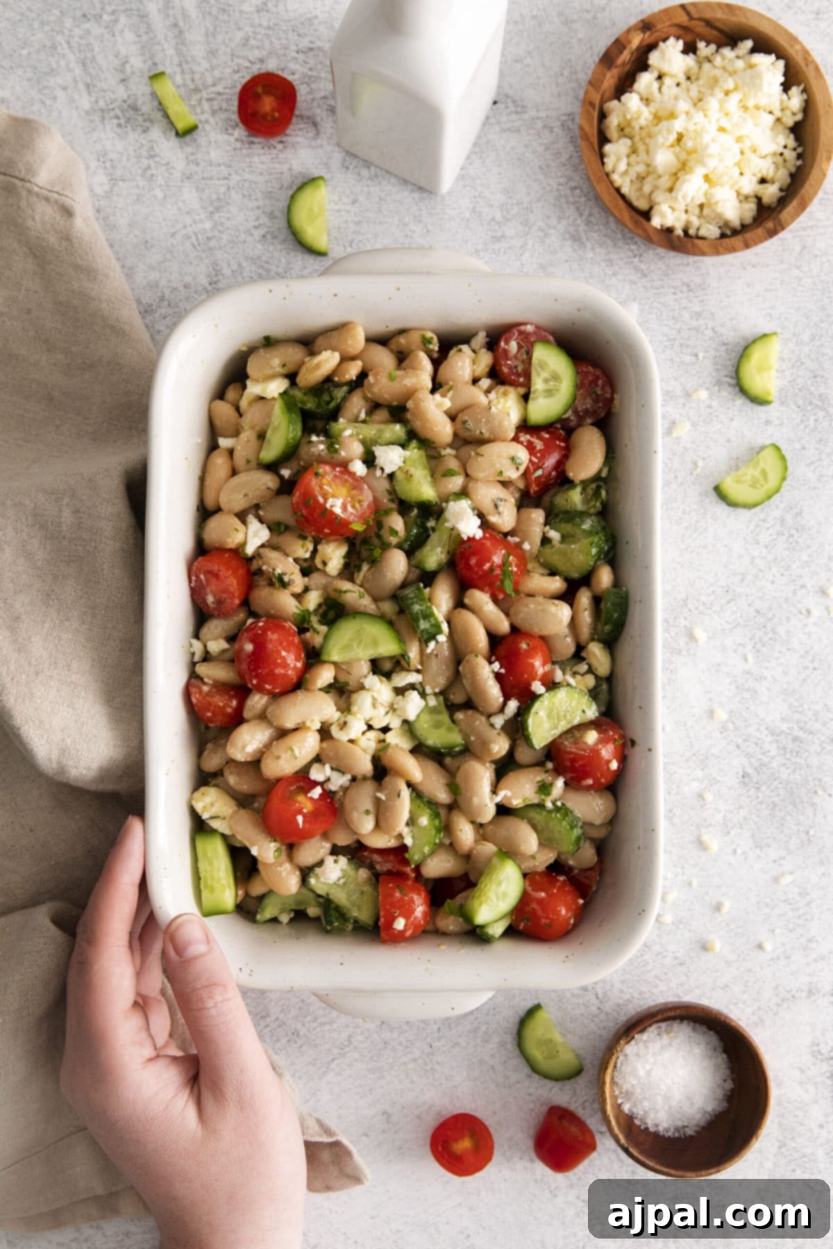 Close-up of a refreshing white bean salad with visible cucumbers, tomatoes, and crumbled feta cheese in a white ceramic bowl, ready to be served.