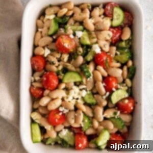 white bean salad in a white bowl with cucumber, tomatoes, and crumbled cheese, perfect for a Mediterranean meal.