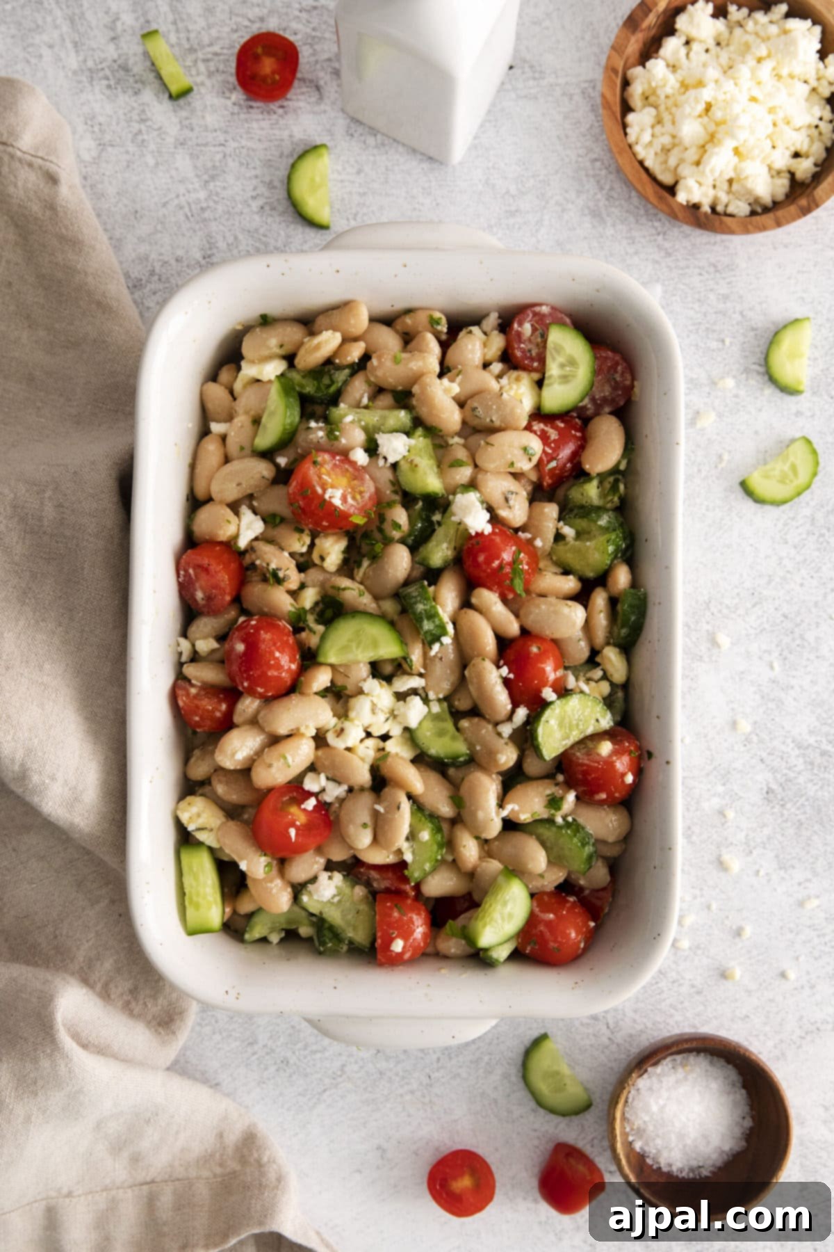 A close-up of a refreshing Mediterranean white bean salad with creamy feta, crisp cucumbers, and juicy tomatoes in a pristine white bowl, showcasing its fresh ingredients.