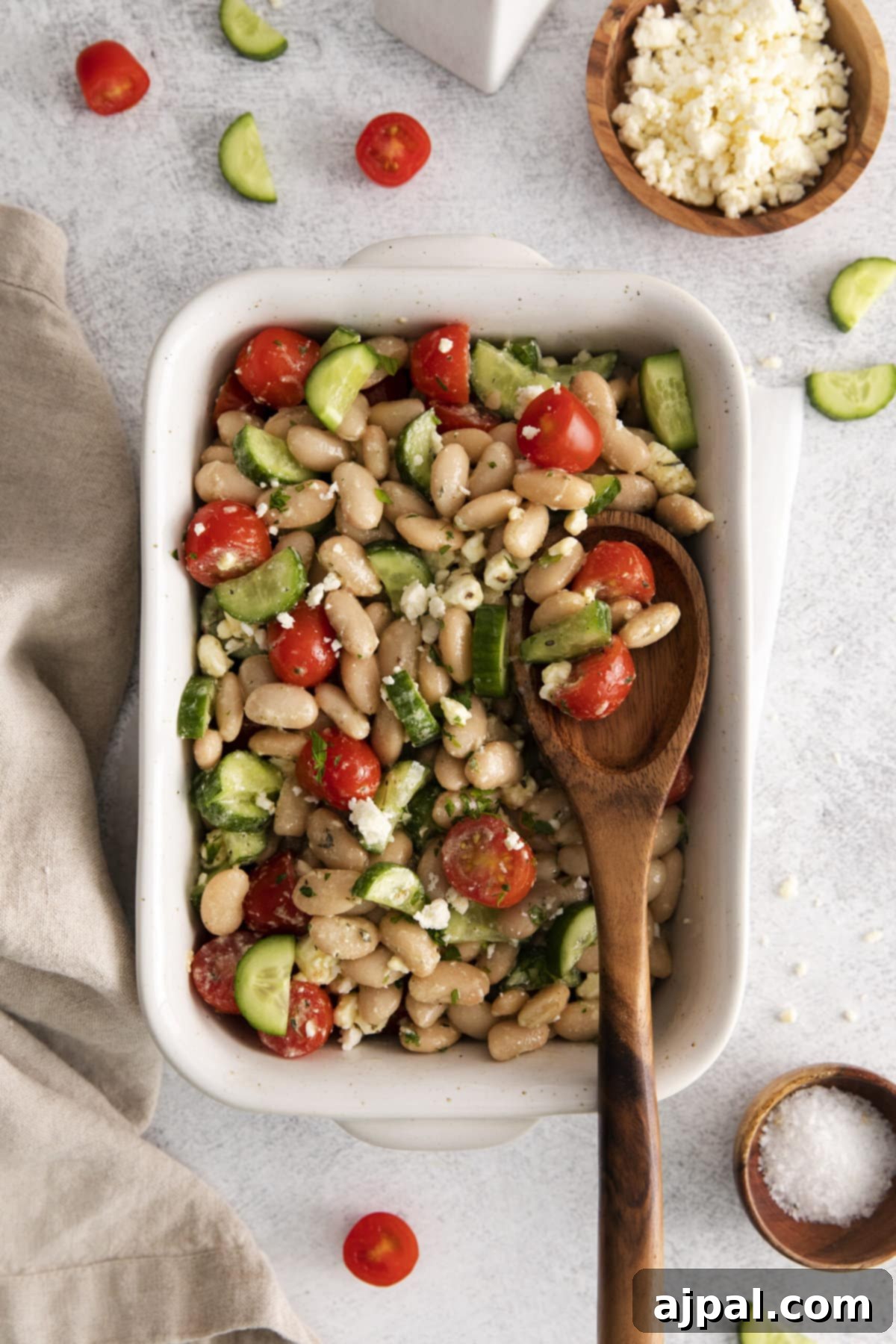 A vibrant Mediterranean white bean salad with cherry tomatoes and cucumber, elegantly dressed with crumbled feta cheese in a white serving bowl, showcasing its delicious freshness.