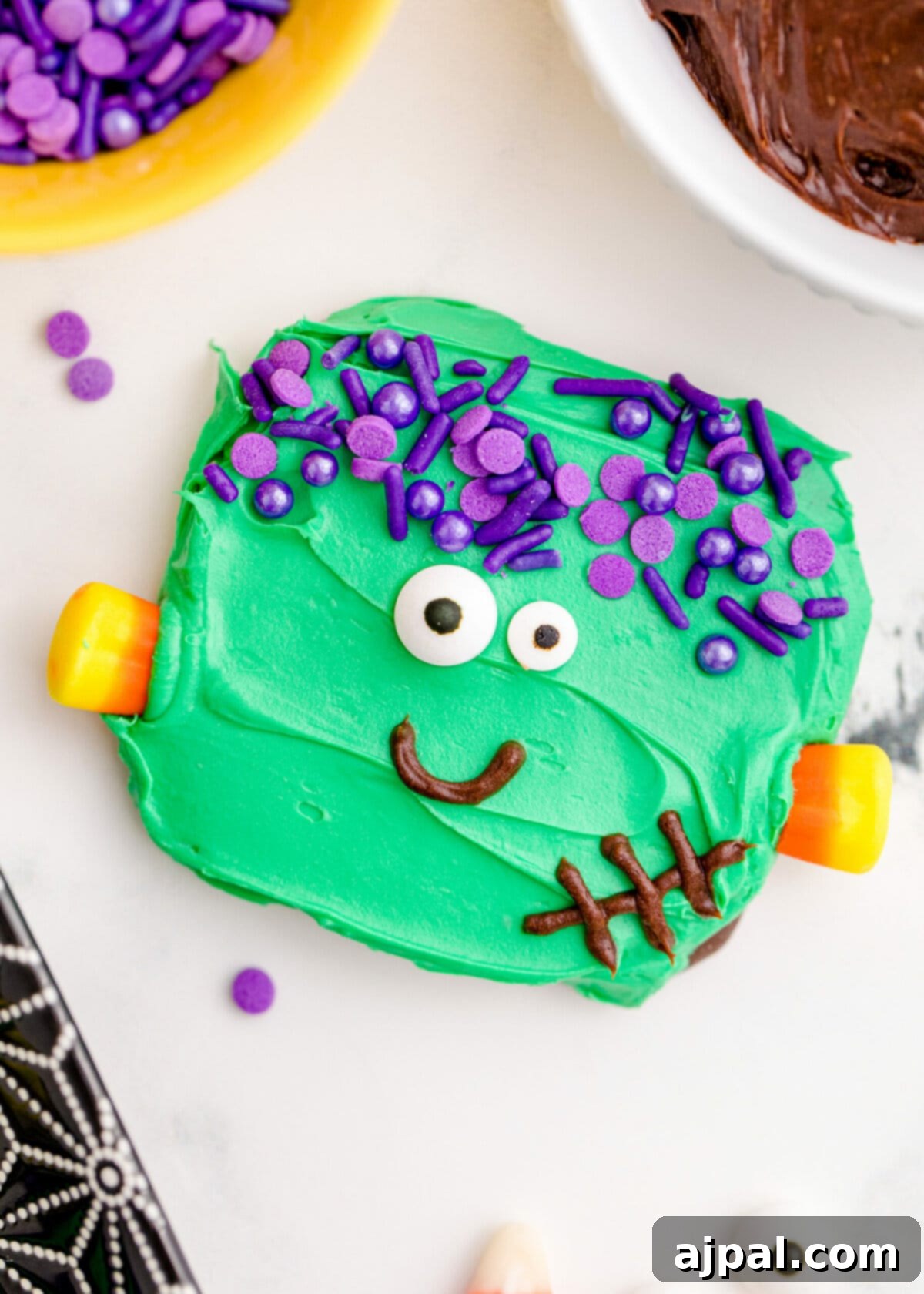 Spooky Frankenstein Cookies 2 Close-up picture of an adorable Frankenstein cookie with green icing, purple sprinkles for hair, candy corn neck bolts, candy eyes, and a hand-piped chocolate smile. Perfect for Halloween parties.