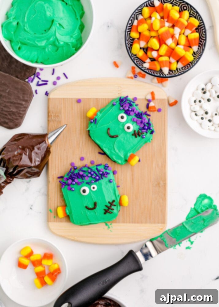Spooky Frankenstein Cookies 12 A collection of ingredients laid out on a table: chocolate-dipped cookies, bowls of chocolate icing, green icing, candy eyes, candy corn, and purple sprinkles, all ready for Frankenstein cookie assembly.