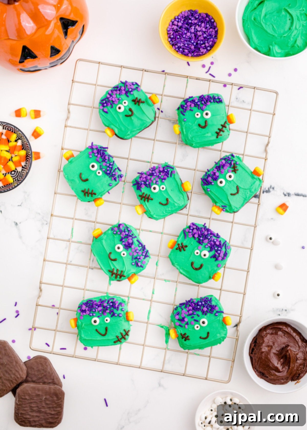 Spooky Frankenstein Cookies 13 A vibrant collection of freshly decorated Frankenstein cookies cooling on a wire rack, ready for a Halloween party, with additional decorations visible in the background.