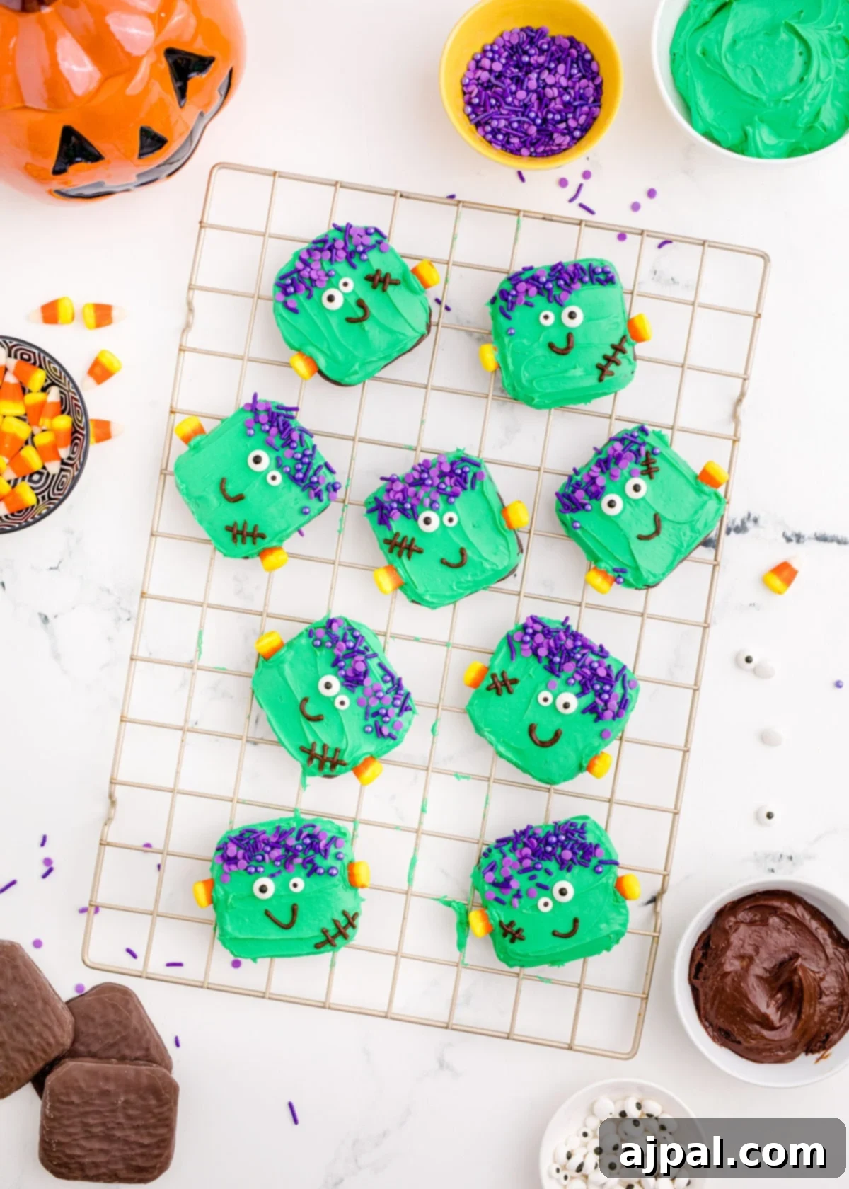 Frankenstein Cookies 5 A selection of Frankenstein cookies, freshly adorned with green icing, sprinkles, and candy decorations, resting on a cooling rack to allow the frosting to set. A collection of colorful candies is visible nearby, emphasizing the festive Halloween theme.