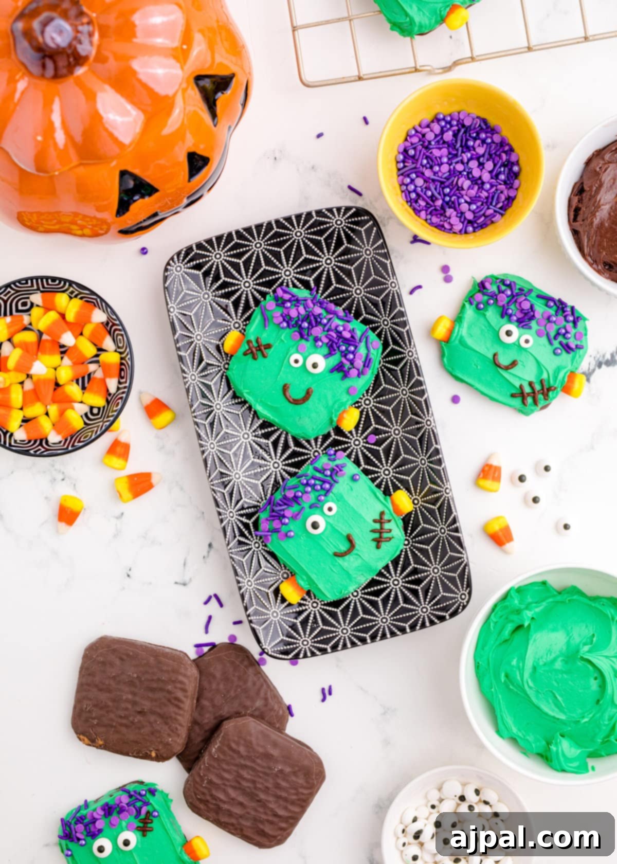 Spooky Frankenstein Cookies 3 A vibrant display of decorated Frankenstein cookies arranged on a serving tray with various Halloween candies, set on a rustic wooden table.
