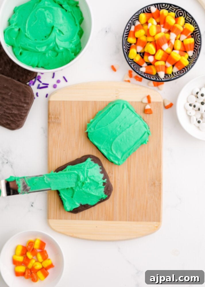 Spooky Frankenstein Cookies 6 A chocolate-dipped cookie being generously covered with bright green icing, forming the base for an easy Frankenstein cookie.