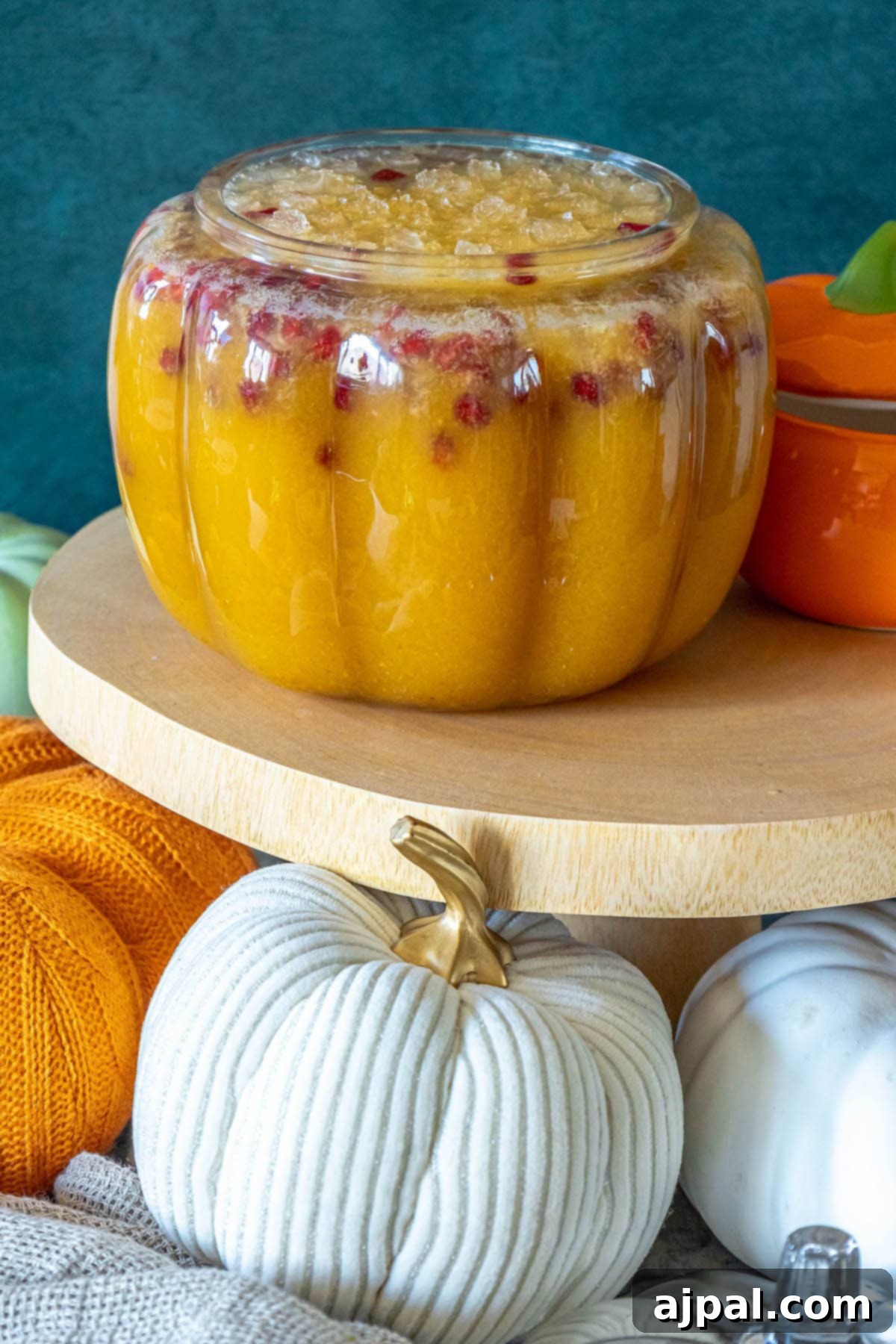 A close-up of a glass of pumpkin punch, garnished with vibrant pomegranate arils and a fresh apple slice, showcasing its festive appeal.
