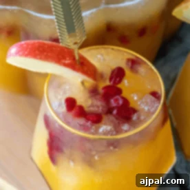 A festive glass of spiked pumpkin pie punch with ice, pomegranate seeds, and an apple slice garnish.