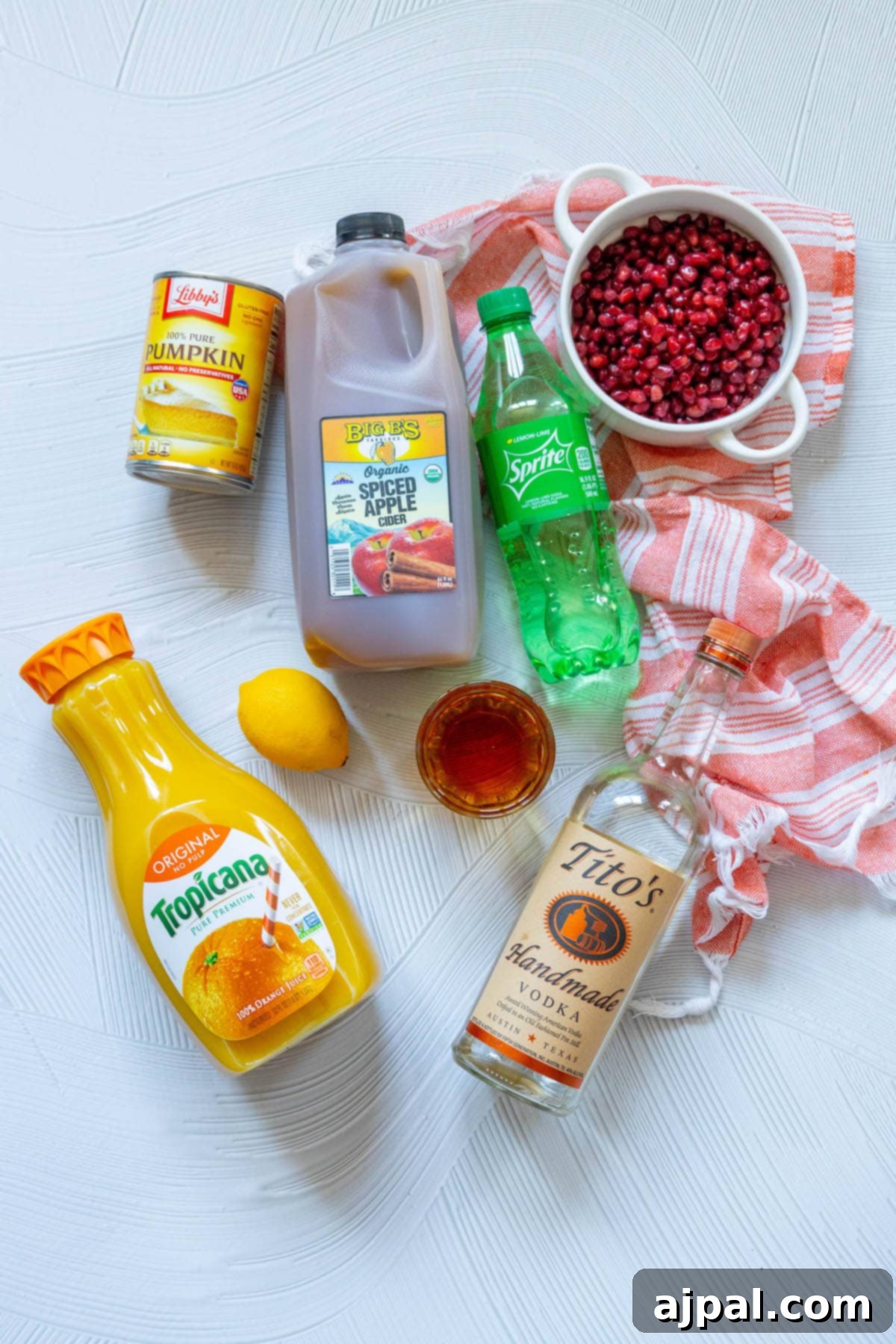 All the ingredients for pumpkin patch punch laid out: brandy, vodka, sprite, pomegranate, pumpkin puree, and apple cider, ready to be mixed.