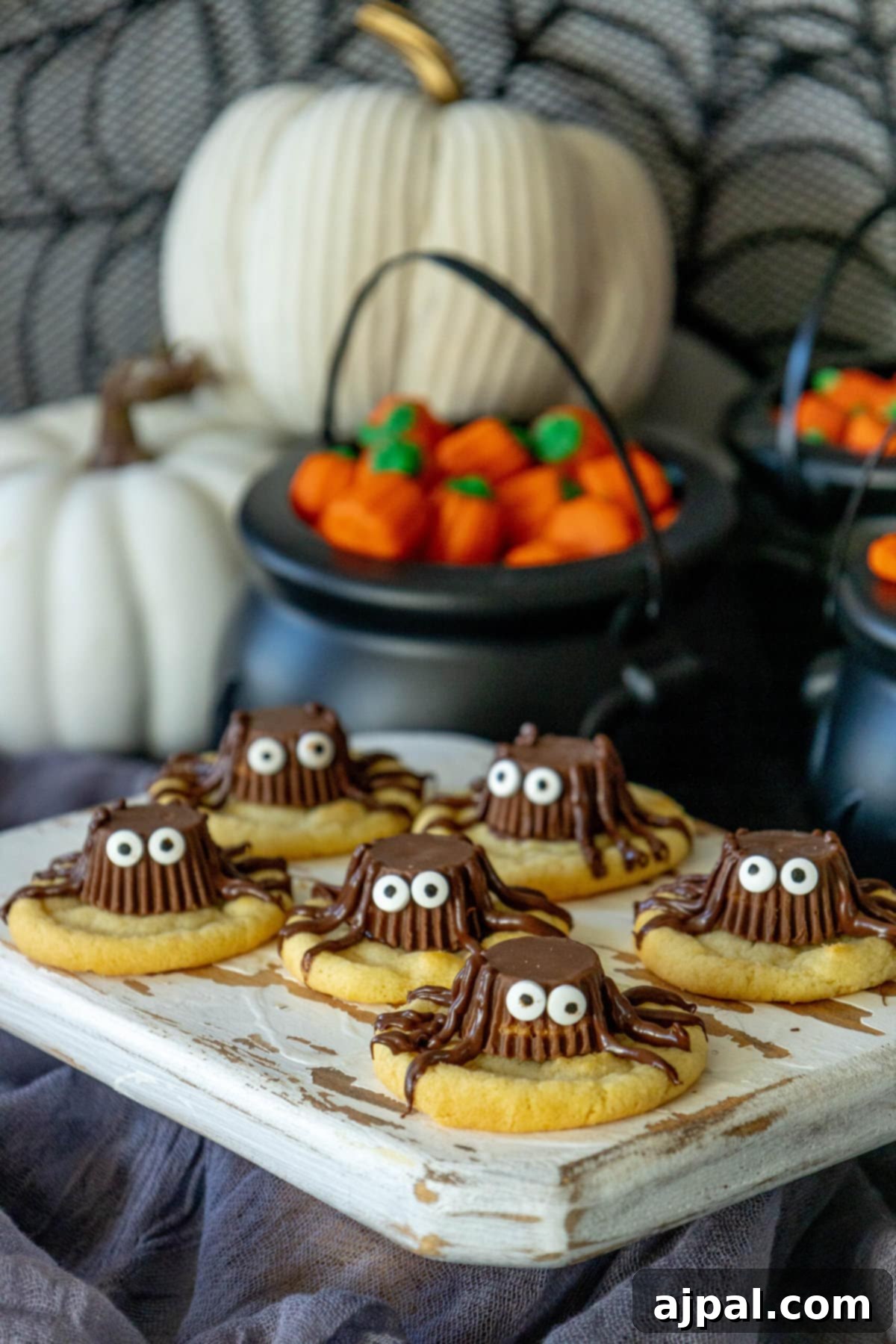 Spooky Spider Cookies 2 Deliciously decorated Halloween spider cookies featuring Reese's Peanut Butter Cups and chocolate legs on a rustic cutting board, surrounded by fall decor.