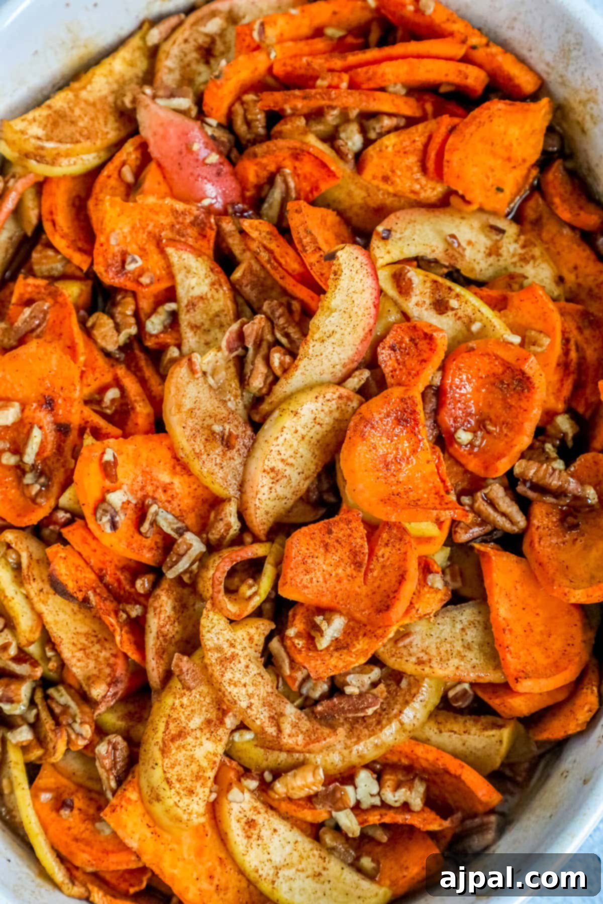 Baked sweet potatoes and apples in a white dish with cinnamon and chopped pecans, ready to serve.