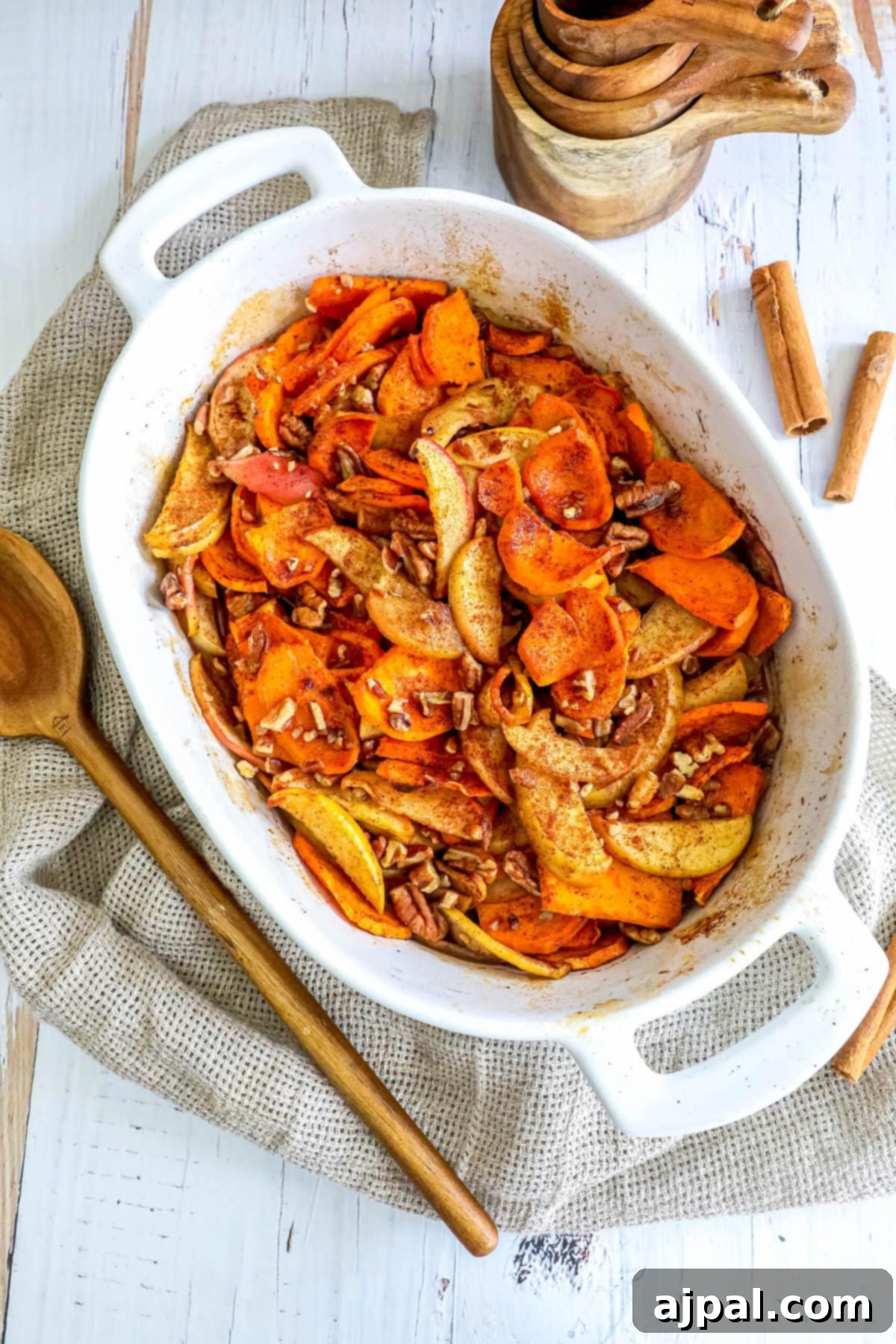 A white dish with perfectly baked sweet potato and apple slices, served with a wooden spoon, highlighting the dish's appealing texture and color.