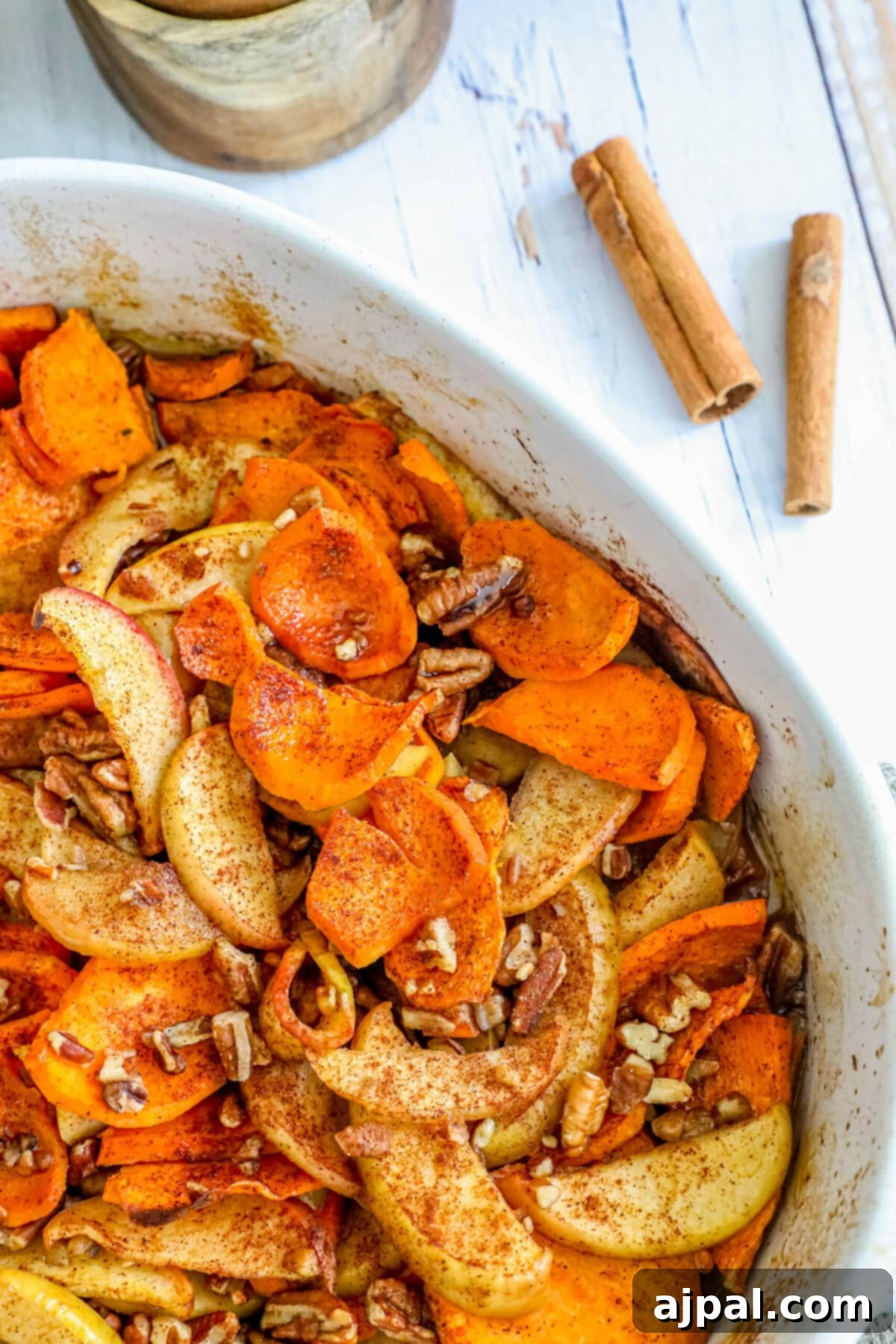 Sweet potato casserole with apples, cinnamon, and a crunchy pecan topping in a white baking dish.