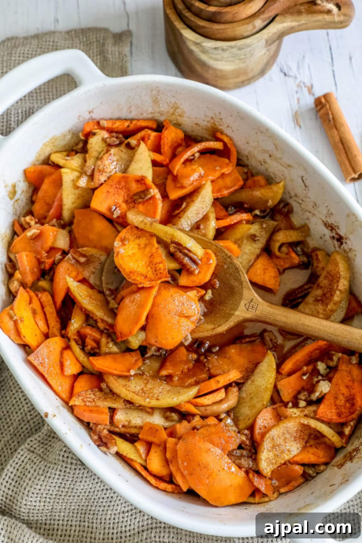 Close-up of roasted sweet potatoes and apples in a white baking dish, showing caramelized edges and cinnamon dusting.