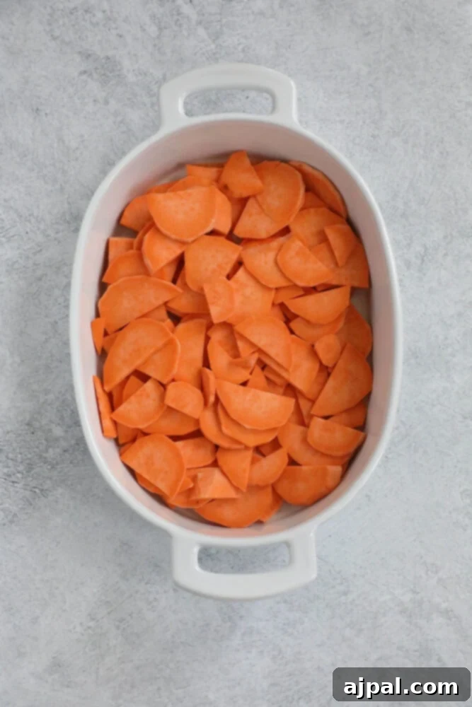 Sliced sweet potatoes neatly arranged in a baking dish, ready for other ingredients.