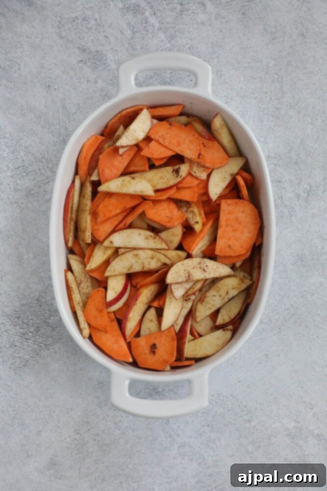Apples and sweet potatoes seasoned with olive oil and cinnamon, mixed in a baking dish before baking.