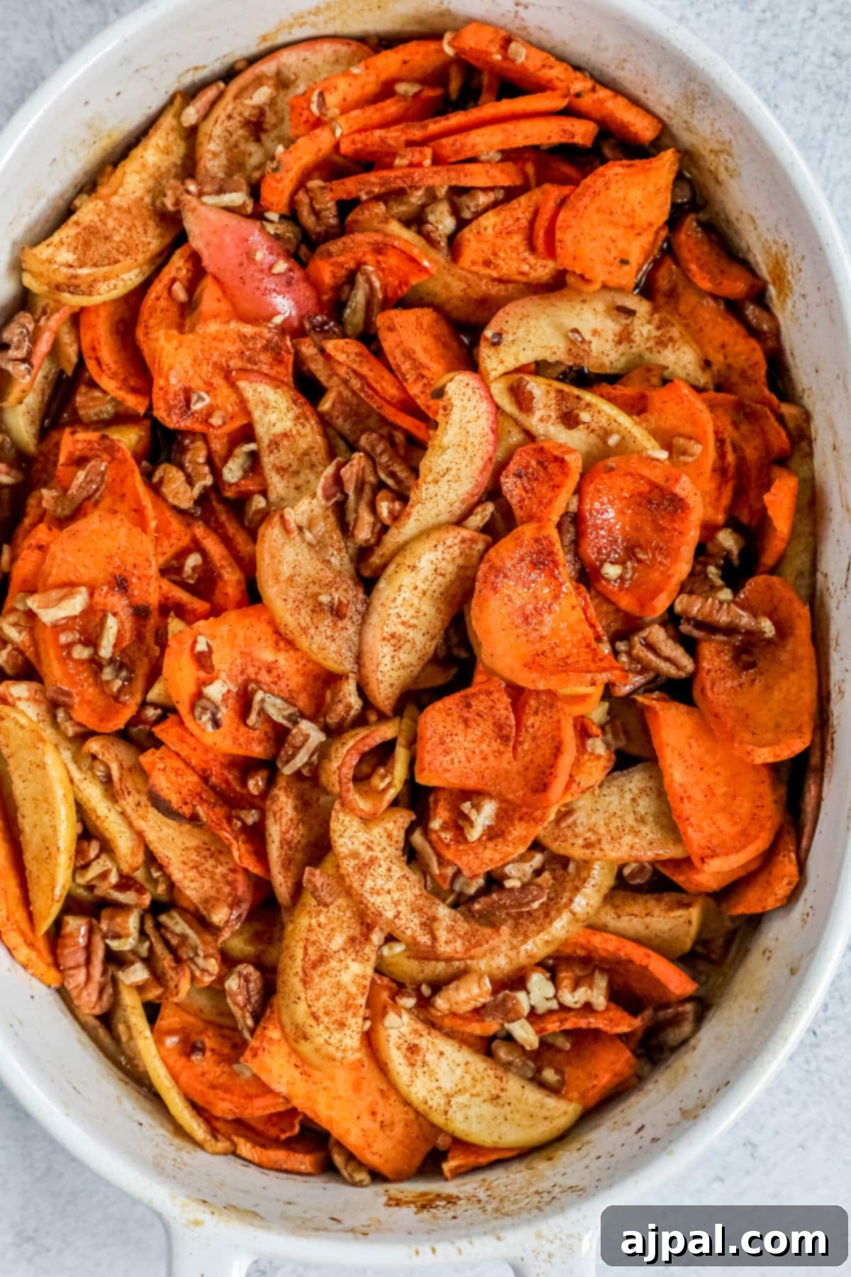 A baked apple and sweet potato casserole in a white dish, garnished with cinnamon and pecans, ready to be served.
