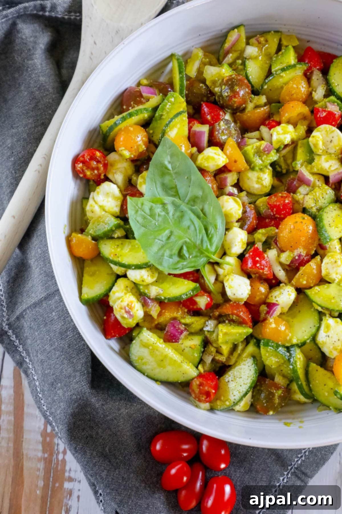 Vibrant Pesto Caprese 2 Chopped cucumbers, cherry tomatoes, red onion, crumbled feta cheese, and fresh basil leaves in a white bowl, generously tossed in homemade pesto sauce.