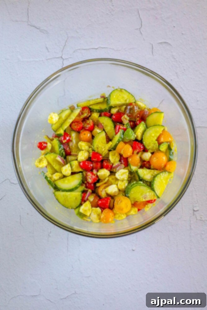 Vibrant Pesto Caprese 8 Diced cucumber, red onion, grape tomatoes, feta cheese, avocados, and fresh basil leaves perfectly mixed with pesto sauce in a pristine white bowl.