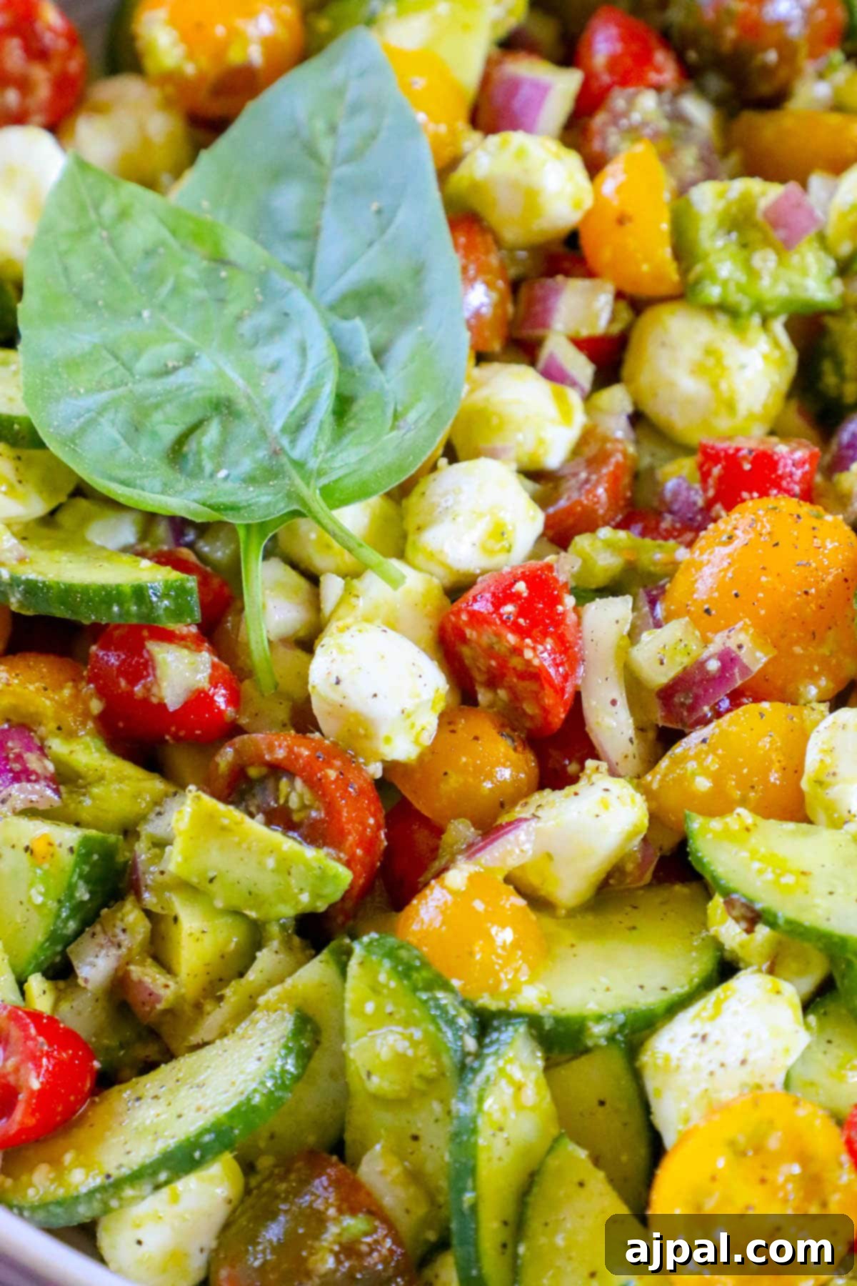 Vibrant Pesto Caprese 10 A visually appealing dish featuring diced cucumber, red onion, grape tomatoes, creamy feta cheese, ripe avocados, and fragrant basil, all perfectly blended with a rich pesto sauce in a white bowl.