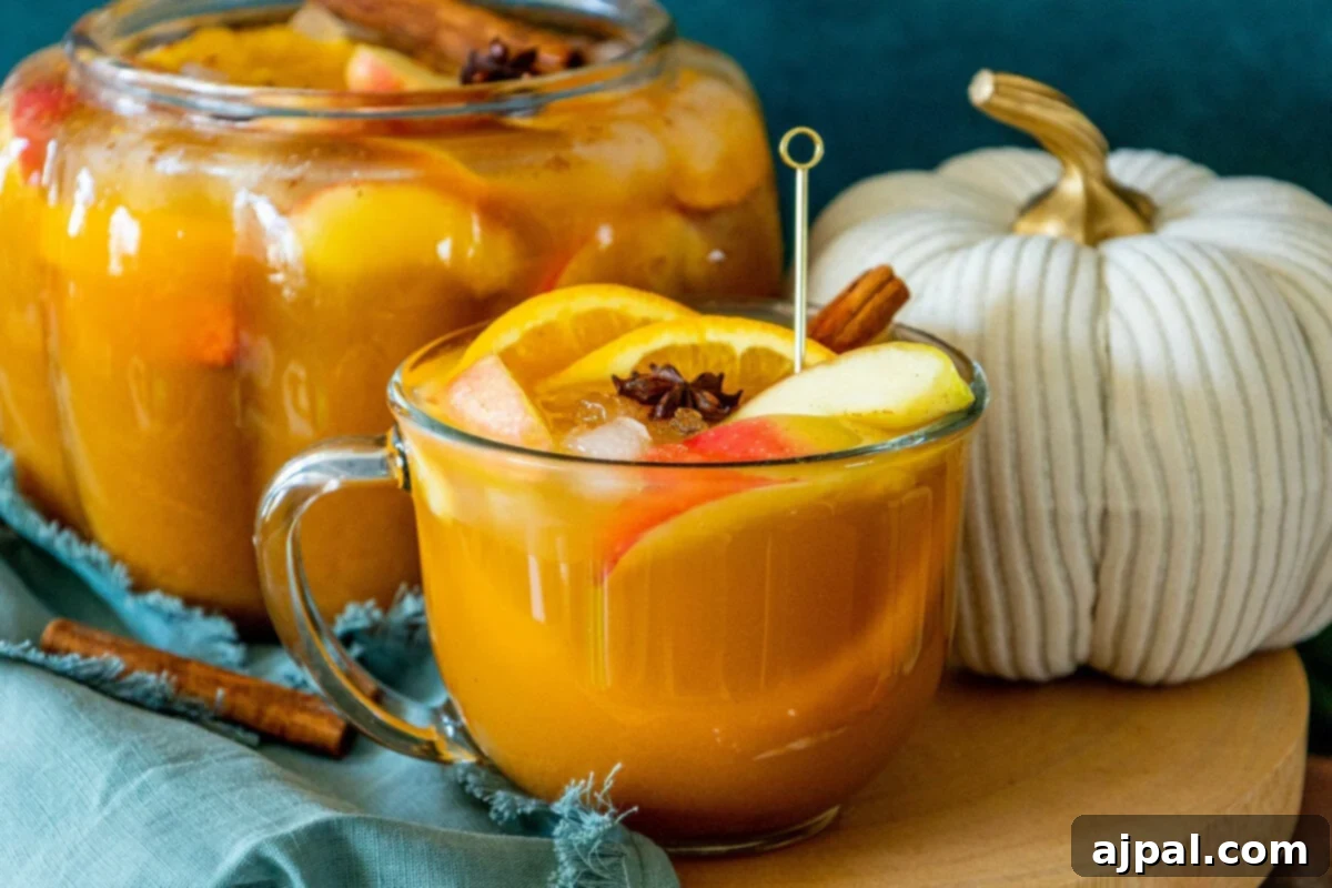 A beautiful glass mug filled with sparkling pumpkin punch, garnished with orange slices, apple slices, a cinnamon stick, ice cubes, and a star of anise, capturing the essence of fall.