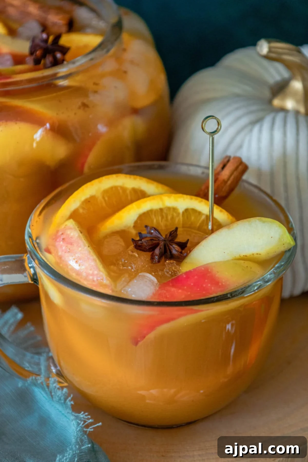 A pitcher brimming with sparkling pumpkin punch, garnished with vibrant cinnamon sticks and fresh apple slices, ready to be served.