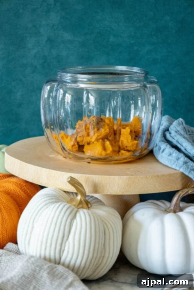 A festive glass jar overflowing with mini pumpkins and white gourds, displayed on a wooden stand, perfect for inspiring autumn pumpkin punch recipes.