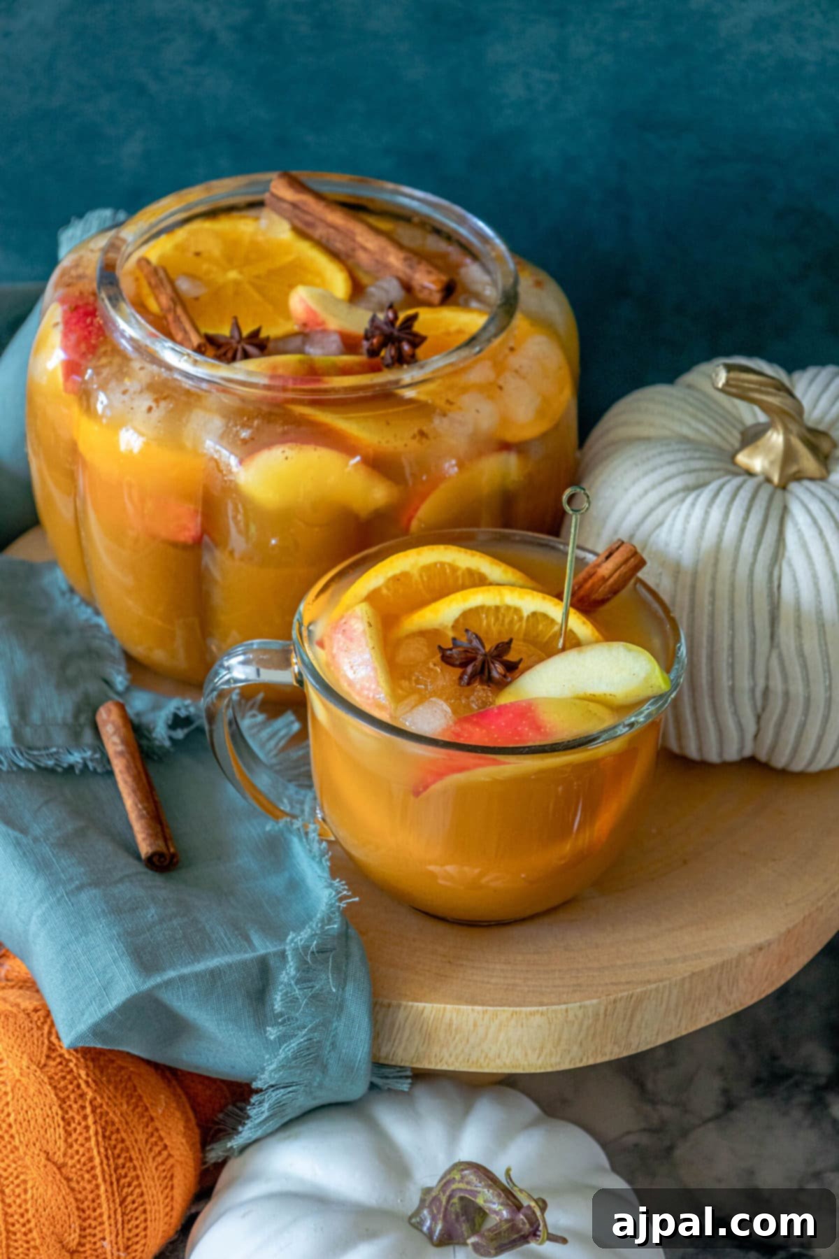 A festive glass of Sparkling Pumpkin Punch garnished with elegant cinnamon sticks and surrounded by decorative pumpkins on a rustic table, ready for a fall celebration.