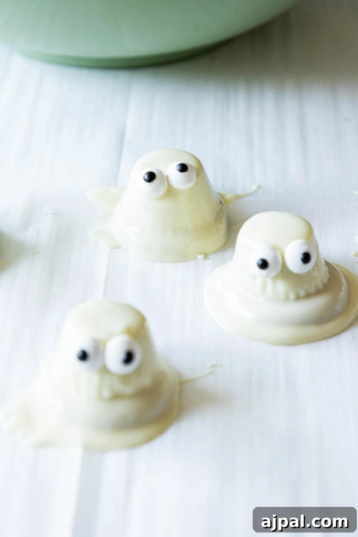 A baking sheet lined with parchment paper, filled with completed white chocolate dipped ghost cookies.