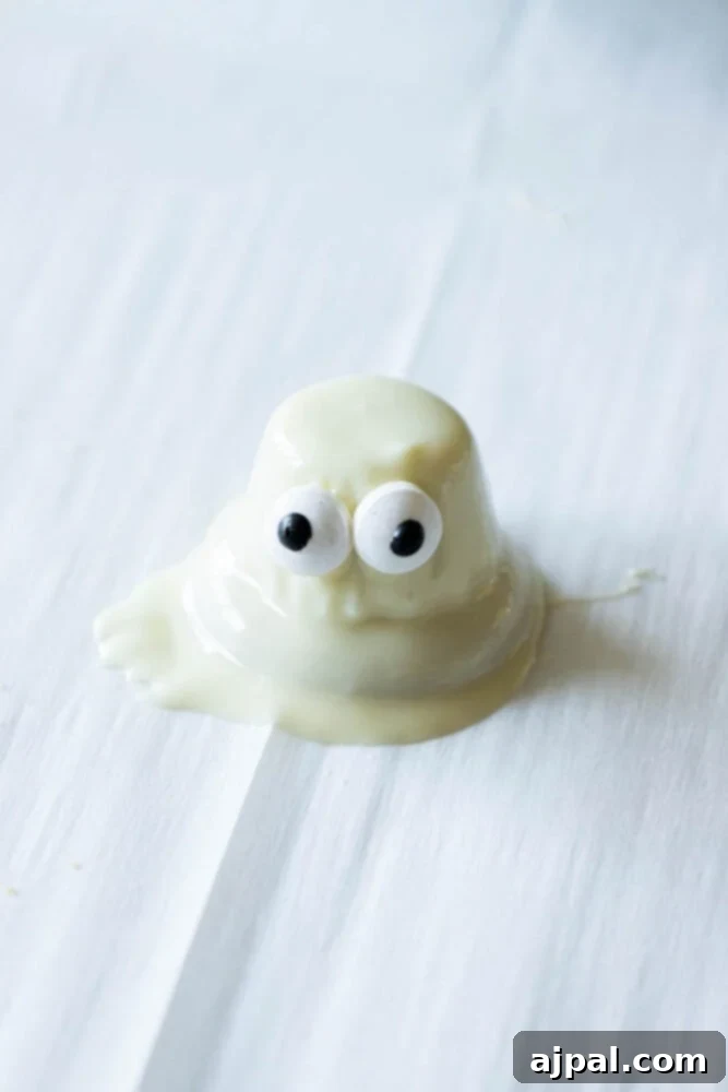 A freshly dipped white chocolate ghost cookie with candy eyes, setting on parchment paper on a baking sheet.