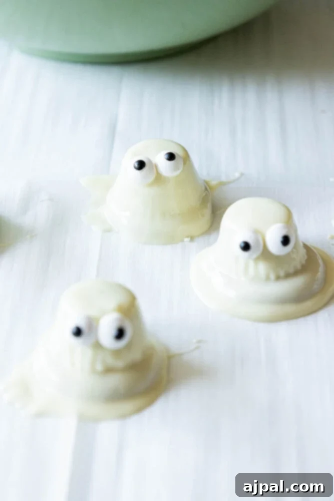 A baking sheet lined with parchment paper, filled with completed white chocolate dipped ghost cookies.