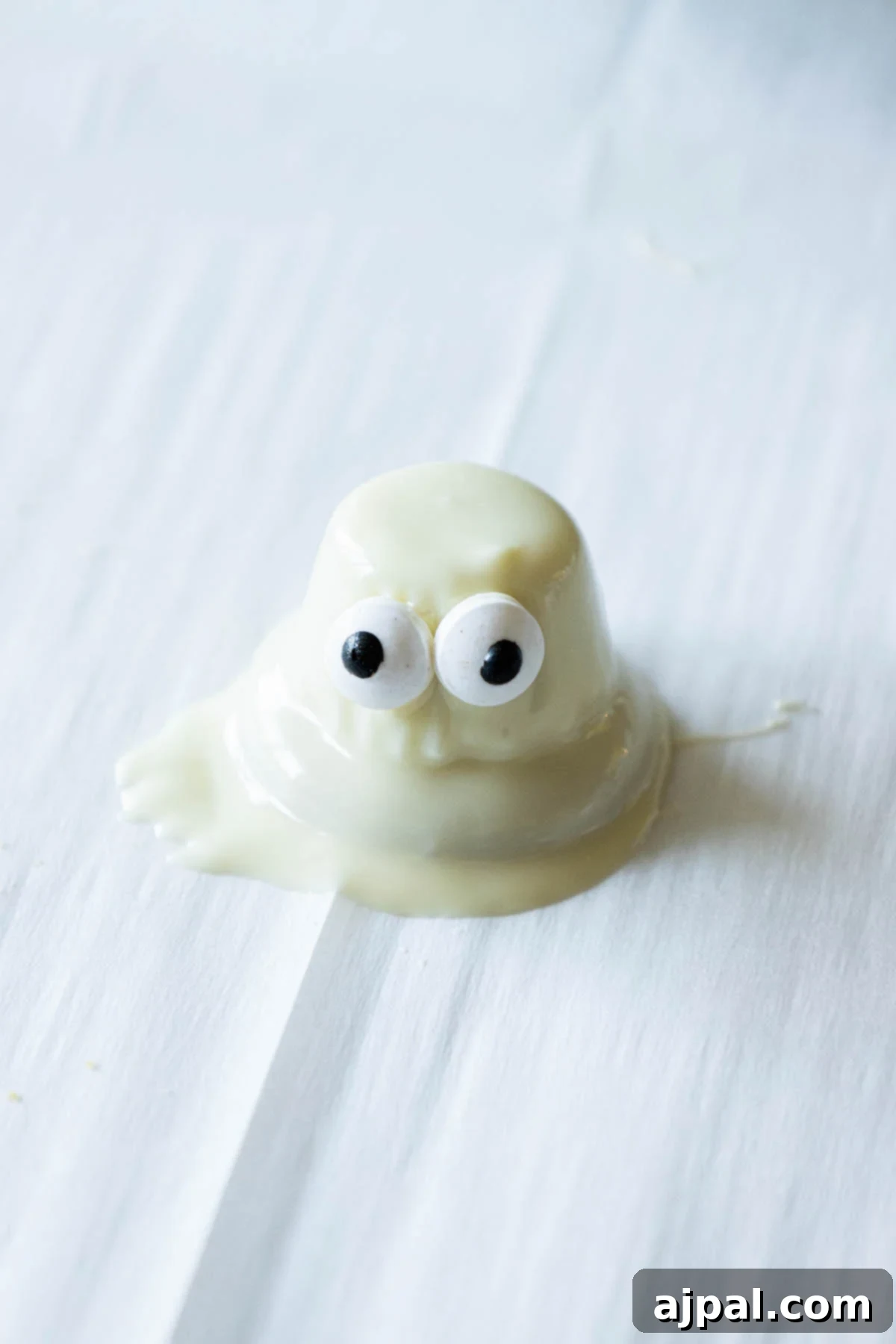 A freshly dipped white chocolate ghost cookie with candy eyes, setting on parchment paper on a baking sheet.