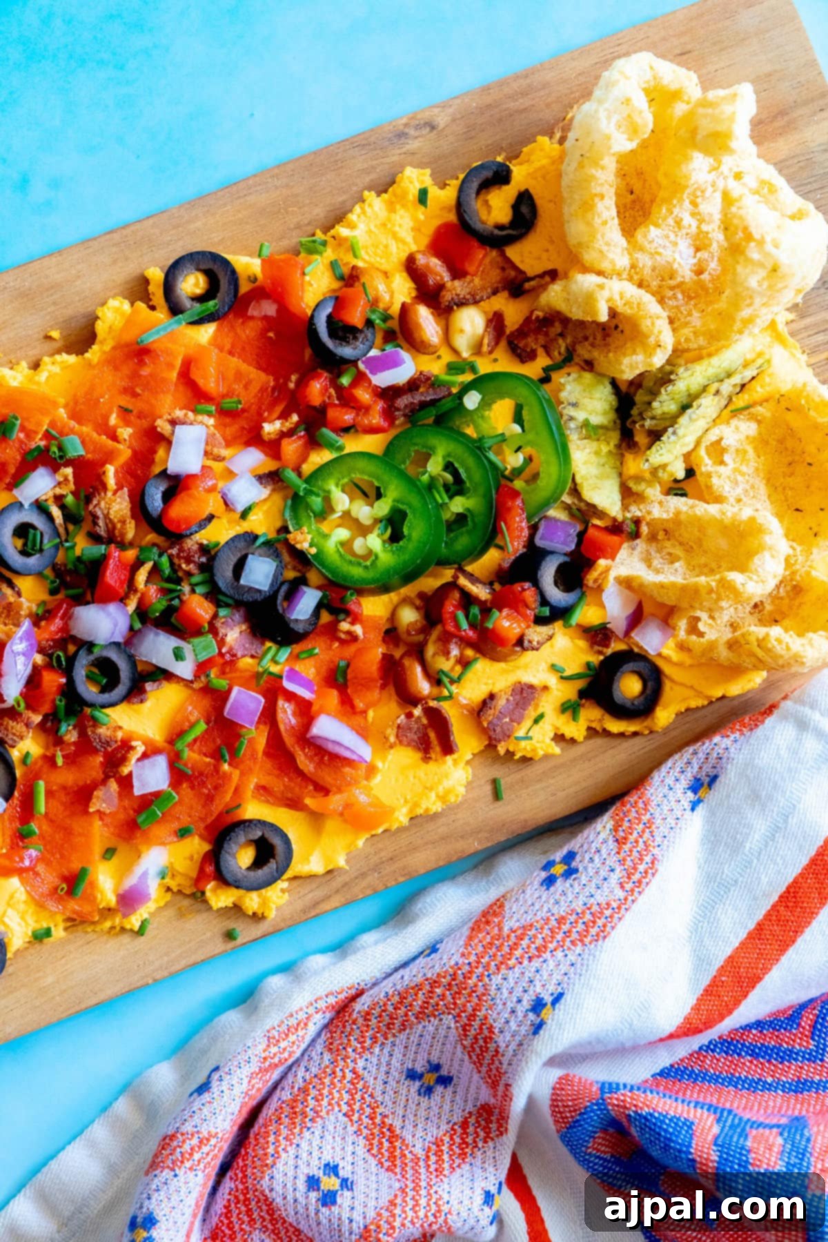 picture of pub cheese spread on a board covered with pork rinds, jalapenos, olives, bacon crumbles, peanuts, pimiento peppers, chives, red onion, and pepperoni