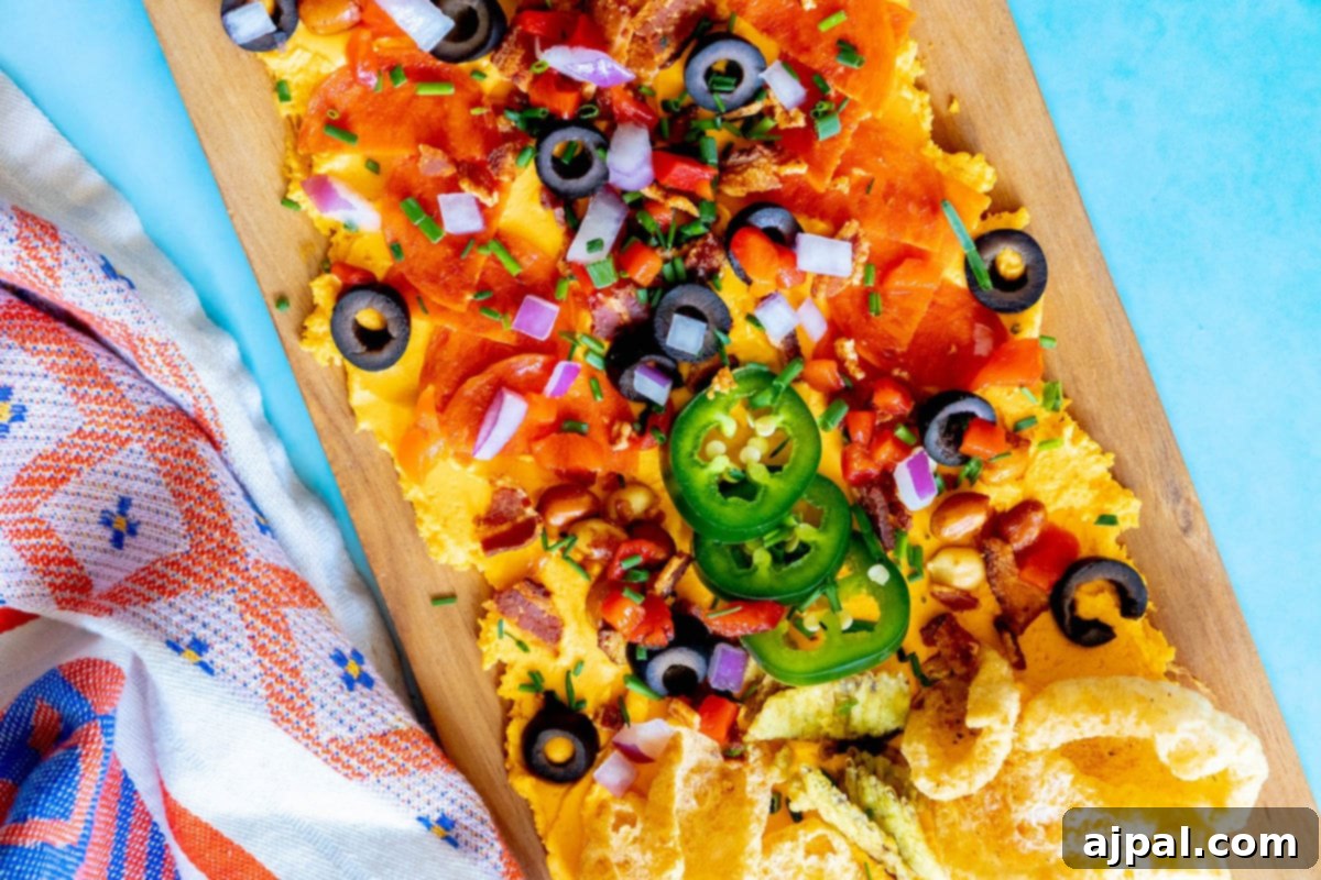 picture of pub cheese spread on a board covered with pork rinds, jalapenos, olives, bacon crumbles, peanuts, pimiento peppers, chives, red onion, and pepperoni